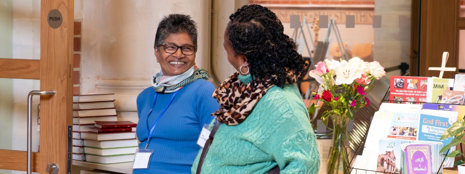 Two women smile warmly at each other in a church foyer