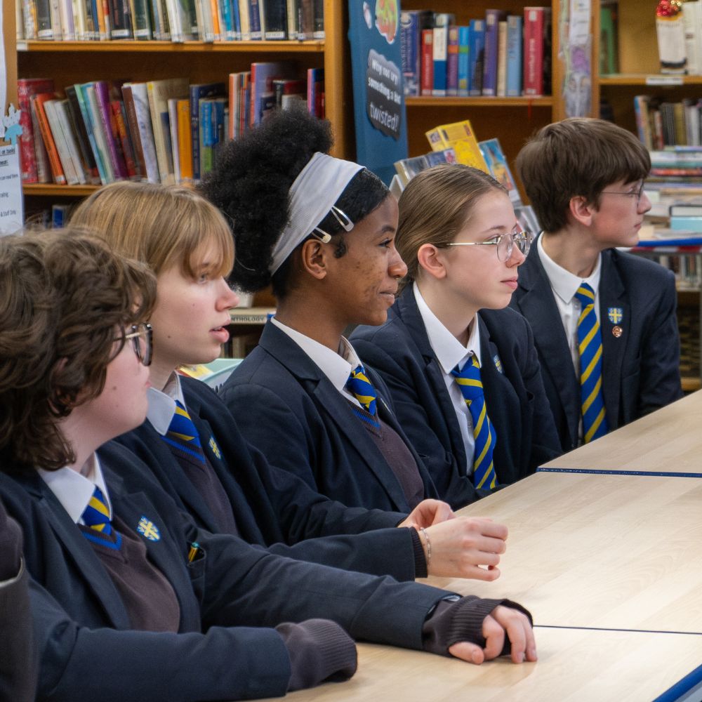 Teenage school students sit in their school library looking at someone out of shot