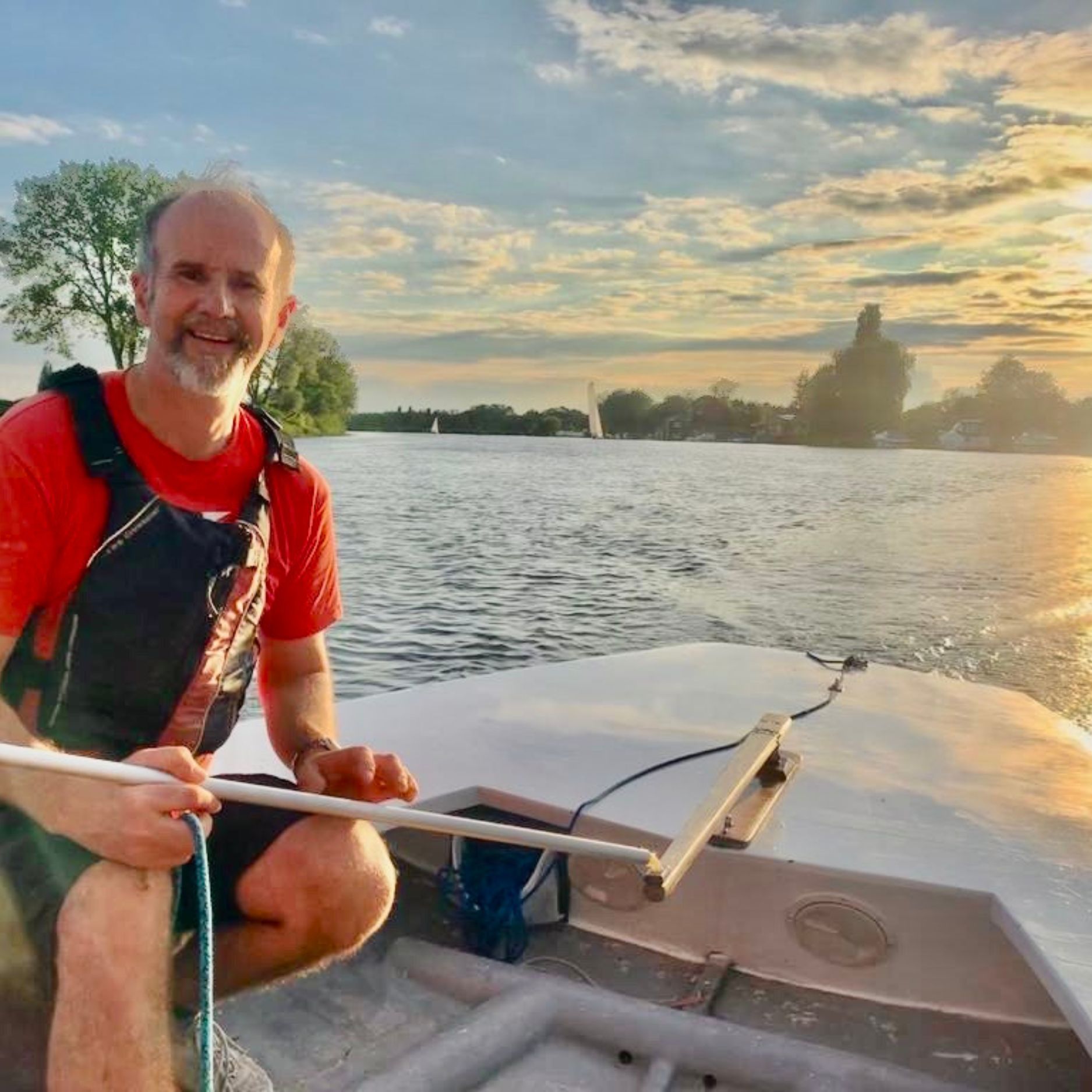 Revd Mark Gould in a Thames A Rater boat, on the river with a sunset in the background.