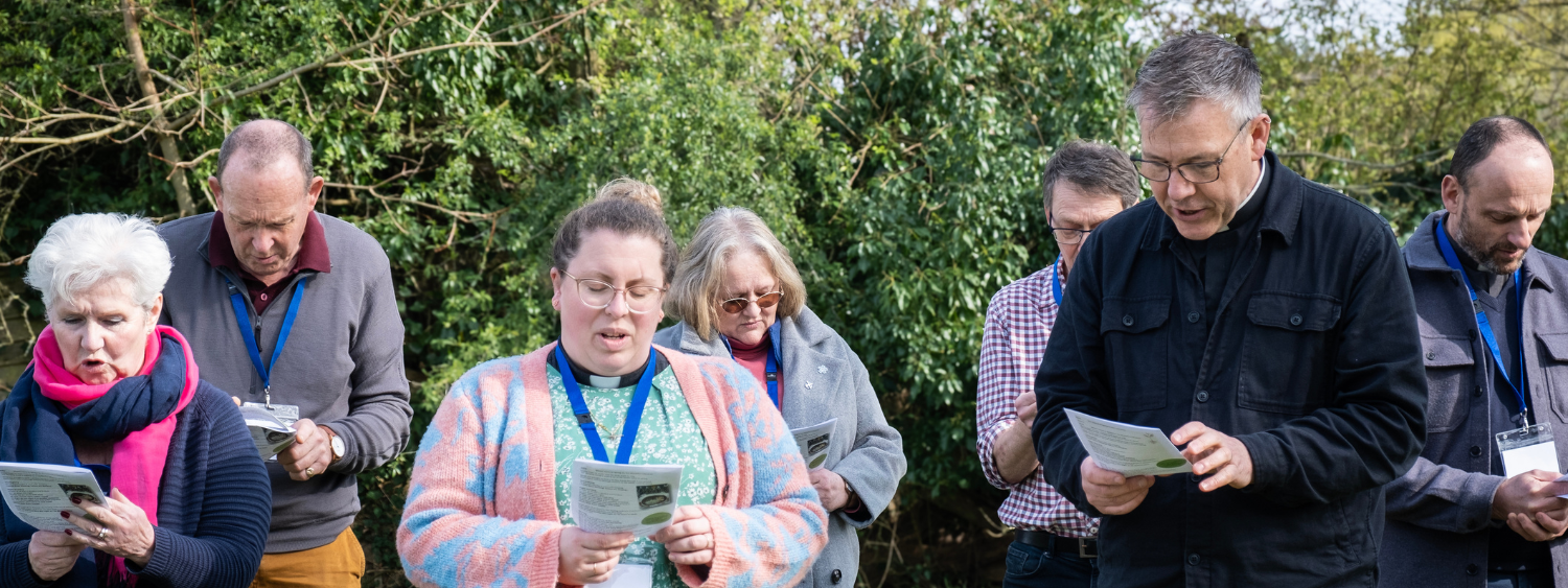 A group of clergy stand in a field, reading from Forest Church liturgy