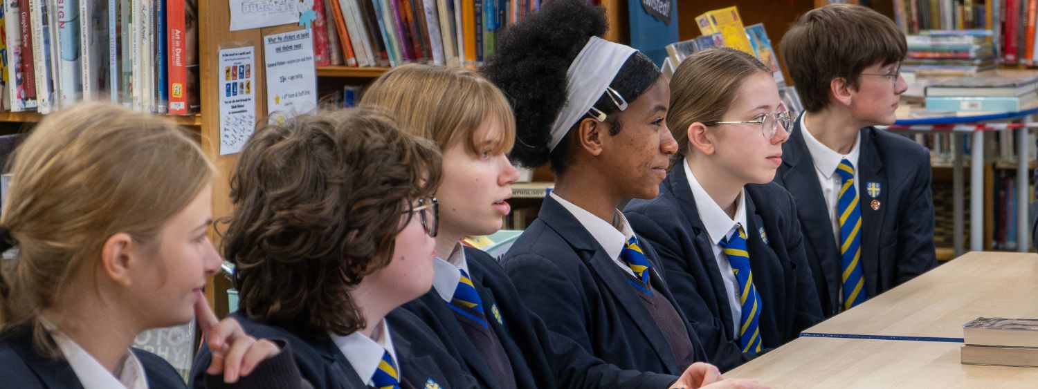 A row of teenage school pupils smile at someone off camera