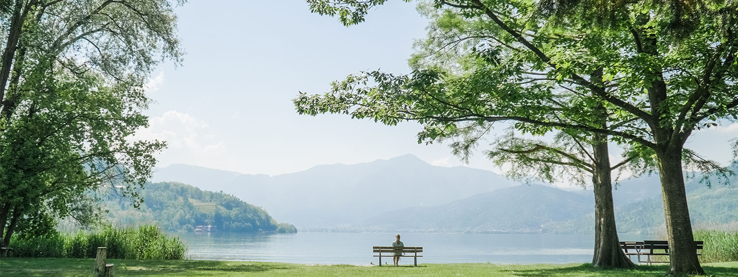 Woman sitting alone on a bench with view over lake and mountains.
