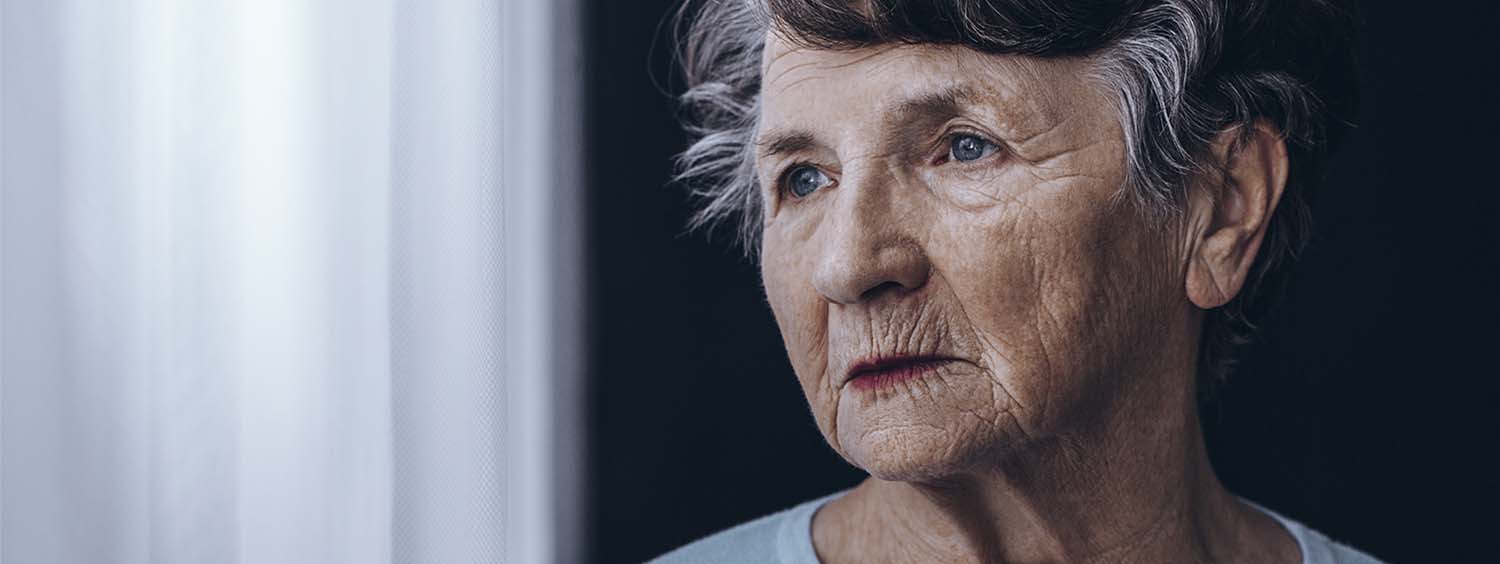 An elderly woman looks out of a window.