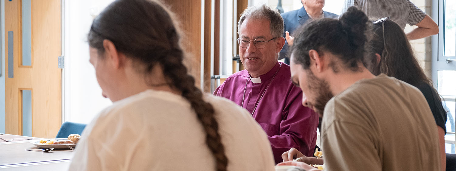 Bishop Steven sits at a canteen table to eat with a group of people