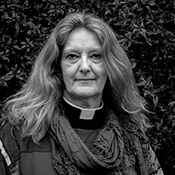 Black and white headshot of the Revd April Beckerleg. April is standing outside smiling, wearing a scarf.