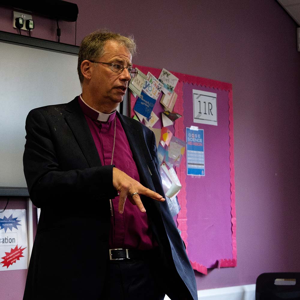 Bishop Steven stands in a secondary school classroom addressing a class of pupils out of shot