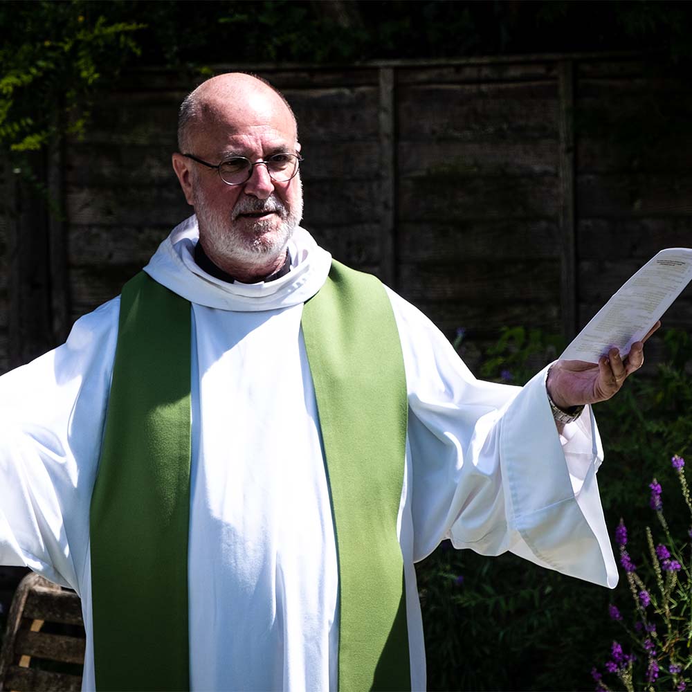 The Revd David Meakin leads an outdoor service. He is wearing white robes and holds his arms out wide