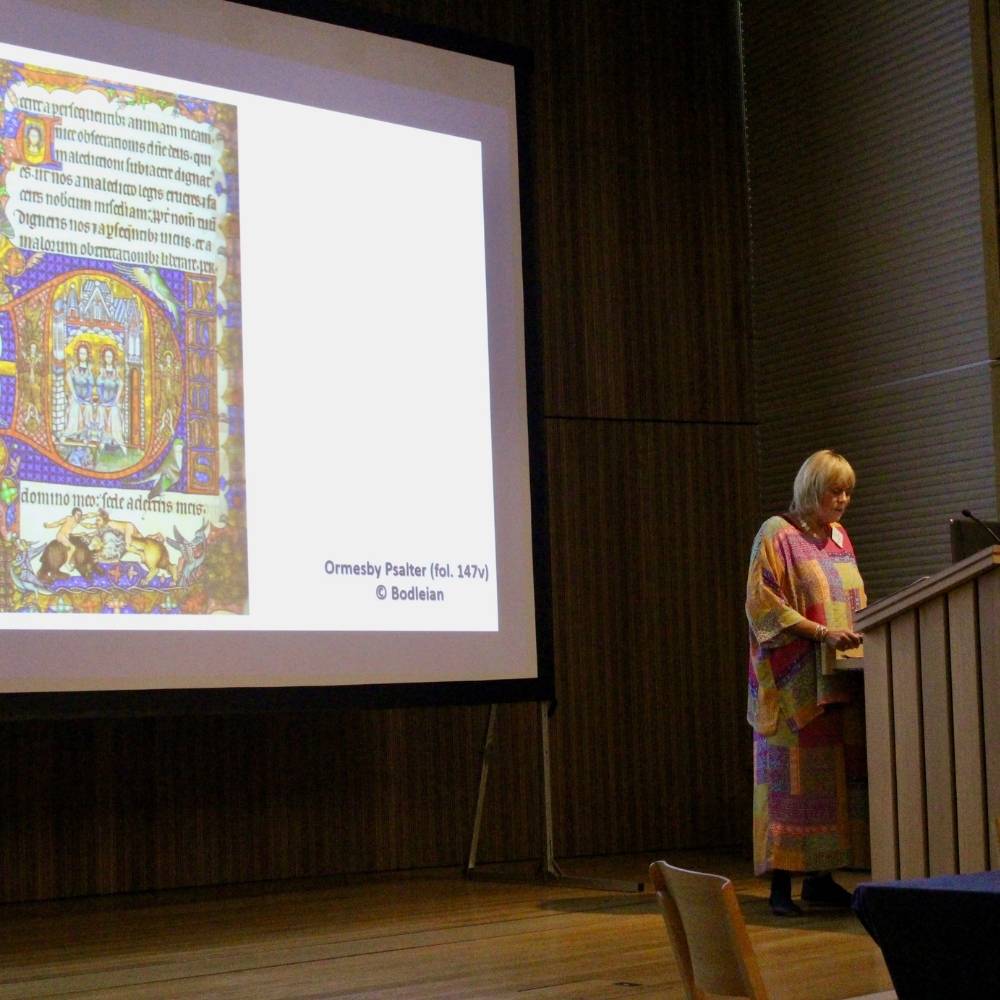 Revd Sue Gillingham stands on a stage at Worcester College infront of a large presentation screen.