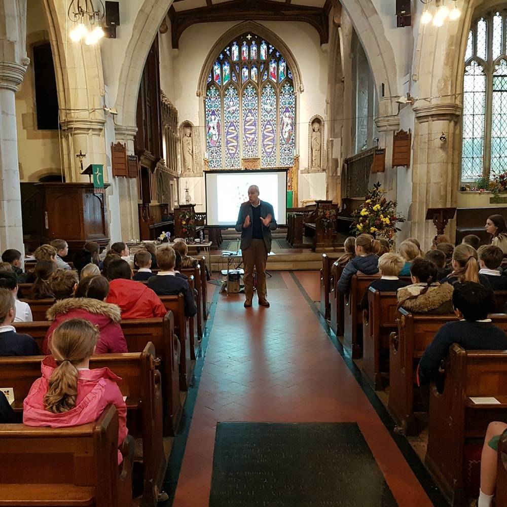 Primary school children sit in church pews facing a man leading a presentation