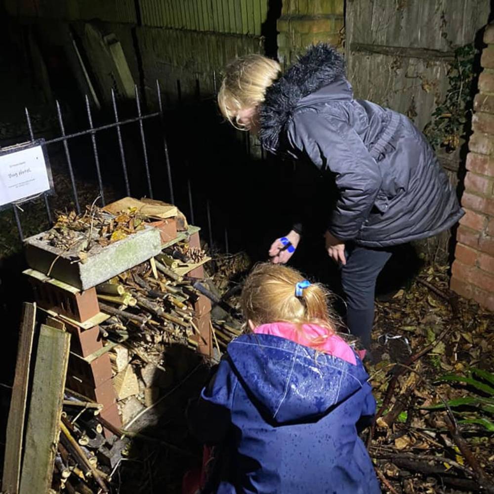 Two young children building a bug hotel in St Peter's churchyard in the dark.