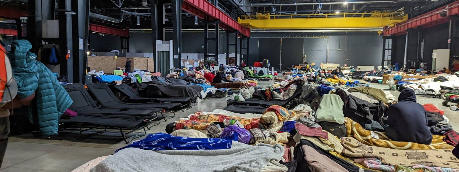 Rows of camp beds belonging to Ukrainian Refugees in a large warehouse in Warsaw with blankets and pillows.