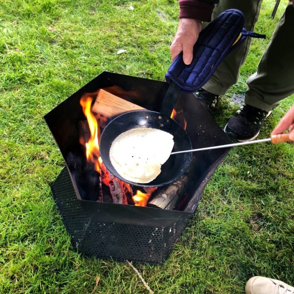 small campfire outside with young person cooking a pancake