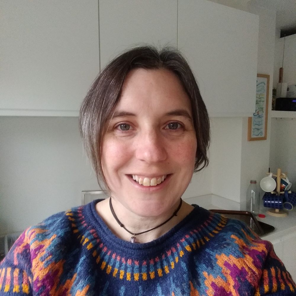 headshot of Gill, she is smiling and wearing a multicoloured jumper.